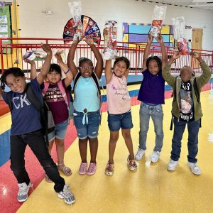 A group of excited children holding bags of food above their heads.