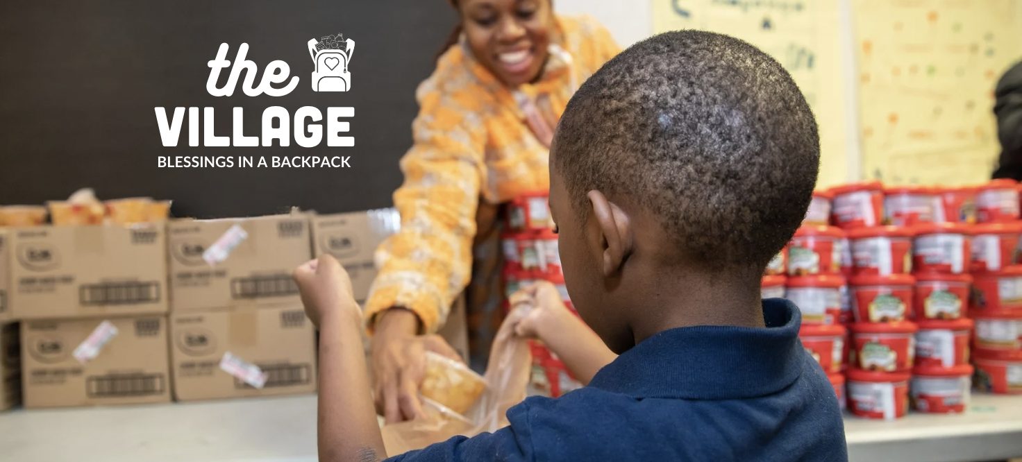 Teacher putting food into a bag with The Village written on the chalkboard